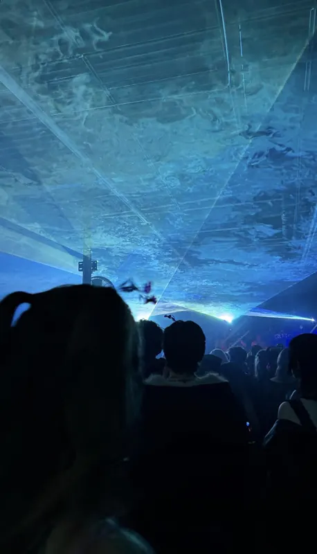 Blue lasers spread across the ceiling above a crowd.