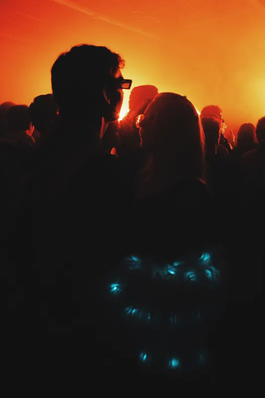 Crowd silhouettes against a bright amber light.