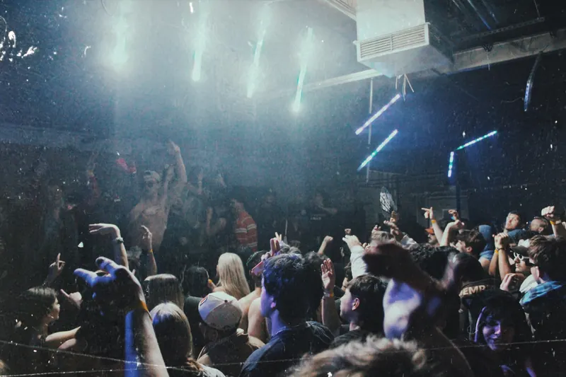 Hands raised in a crowd beneath bright white lights.