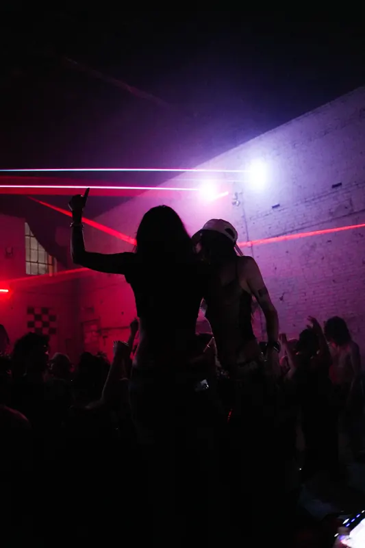 Two silhouettes dance against red lasers and a violet-lit wall.