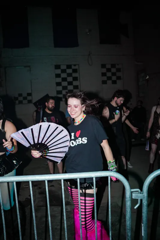 A smiling guest holds an open fan at the front barrier.