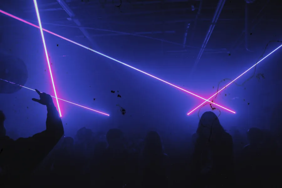 Blue and pink lasers cross above silhouettes on the dancefloor.
