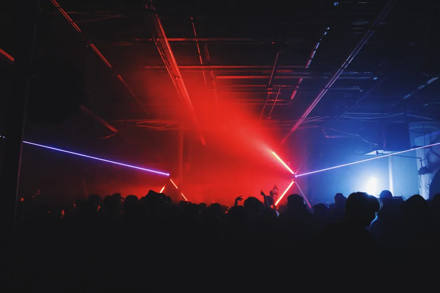 Crowd silhouettes beneath red light and blue lasers.